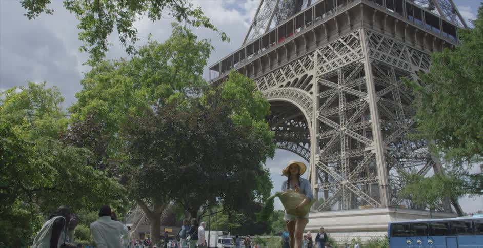 A woman carrying a basket of produce as she walks away from the eiffel tower