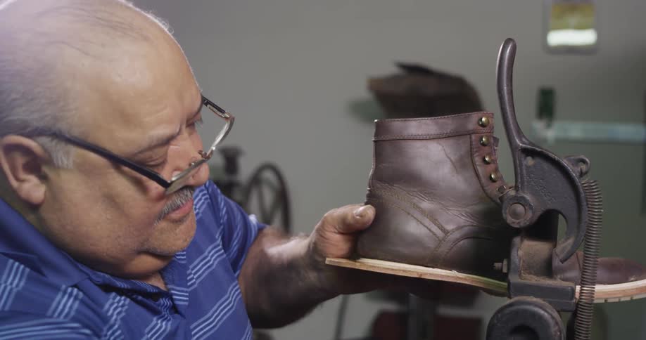 A man in a blue shirt runs a shoe through a machine