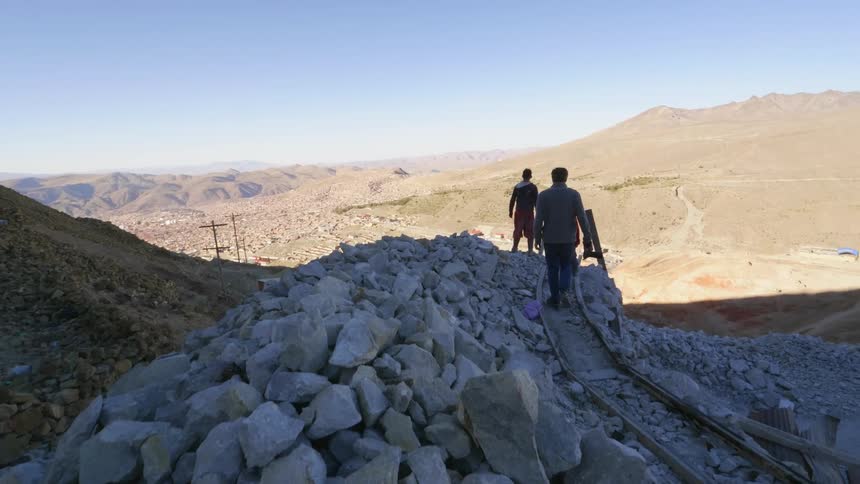 Three men walk up a rocky trail in the mountains under a blue sky