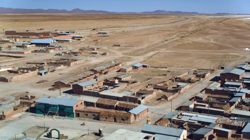 Aerial view of a flat dirt covered area with buildings and a person walking and a person driving a motorcycle