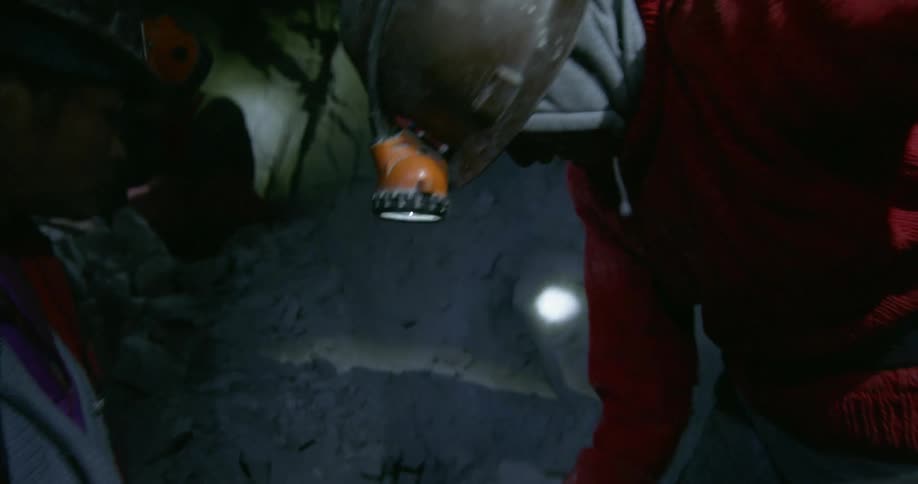 Two men with lights on their helmets dig underground