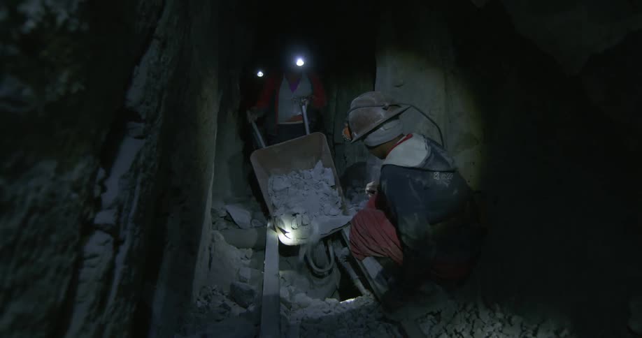 A miner dumps out a wheelbarrow of rocks in a dark mine