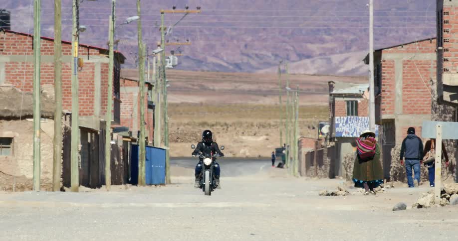 A motorcycle rides past pedestrians in a rural village