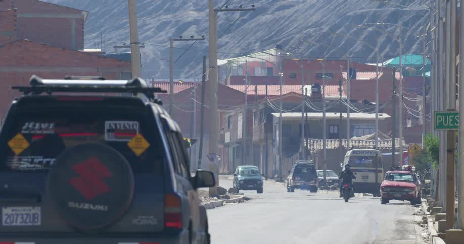 Traffic traveling along a road through a town at the base of a barren mountain
