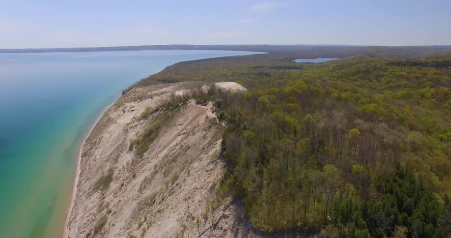 Aerial view of a coast line with a hill leading up to a forest