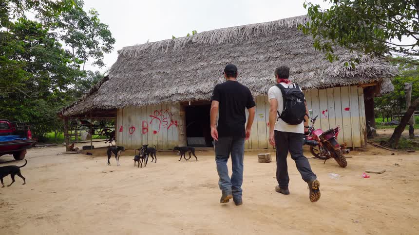 A man carrying a camera walks towards a shack with dogs running every where