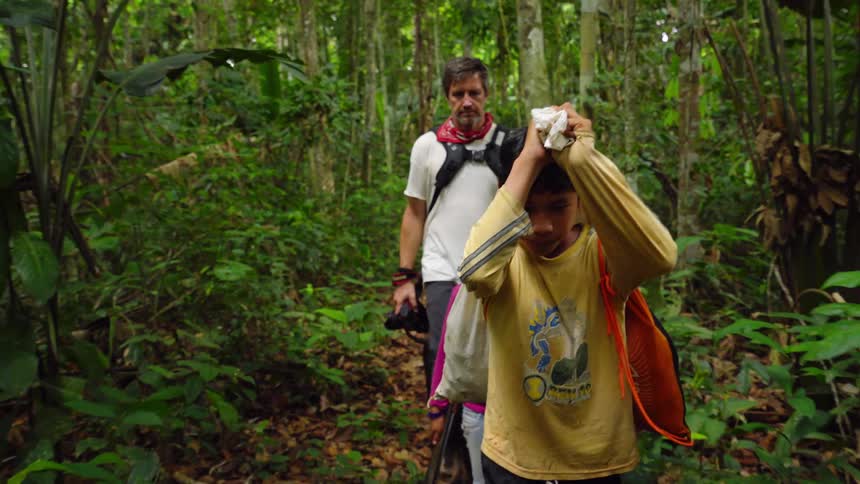 A man carrying a camera walks through a forest with two children