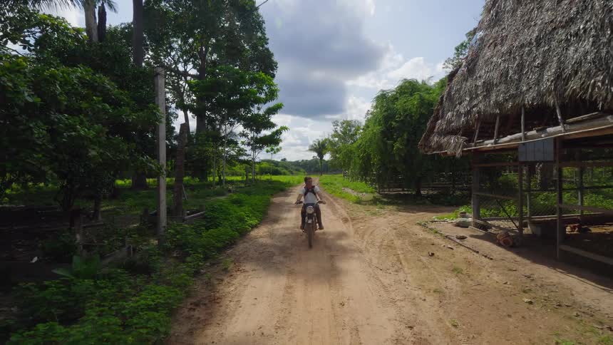 Rider rides a bike on a dirt road near the grass huts