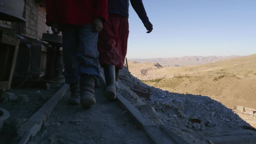 Two men in work clothes walk along a narrow ledge