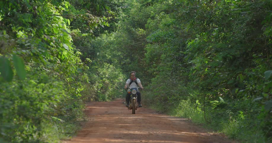 A man rides his motorcycle on the path through the forest