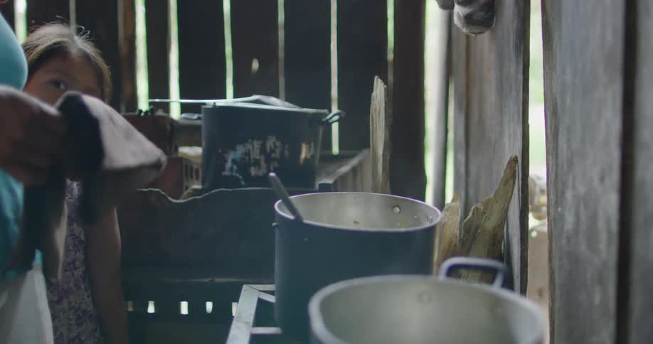 Woman cooking on a stove inside a wooden shack with her daughter