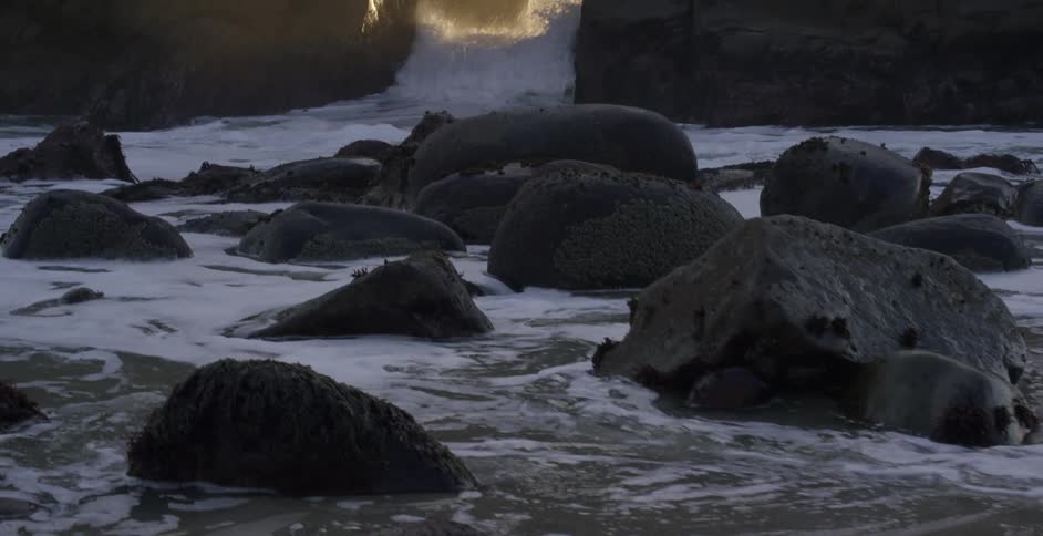Ocean waves was through an opening in a rock formation onto a beach covered in large stones