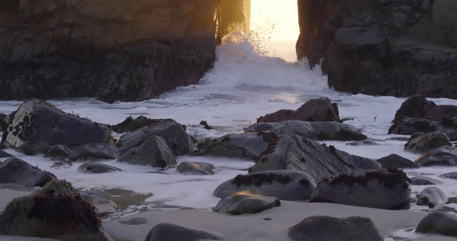 Ocean waves crashing through rock wall at sunset