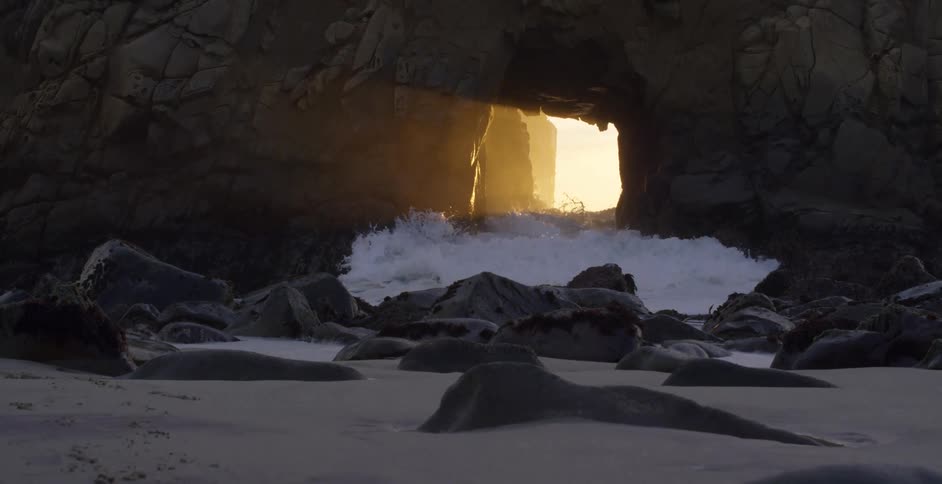 Ocean waves crashing through the rock wall on a beach at sunset