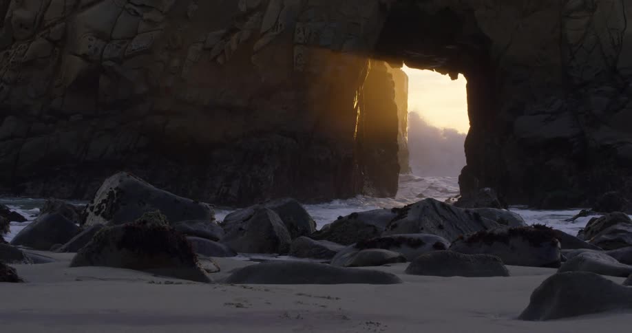 Waves crash against rocks as water flows through short tunnel in cliff