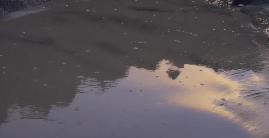 A wet sandy beach with rocks with the reflection of the sky and clouds coming off of it