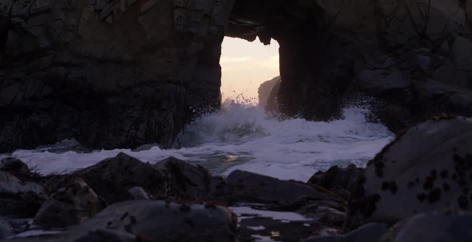 Ocean waves crash in a cave through a large rock formation on the coast