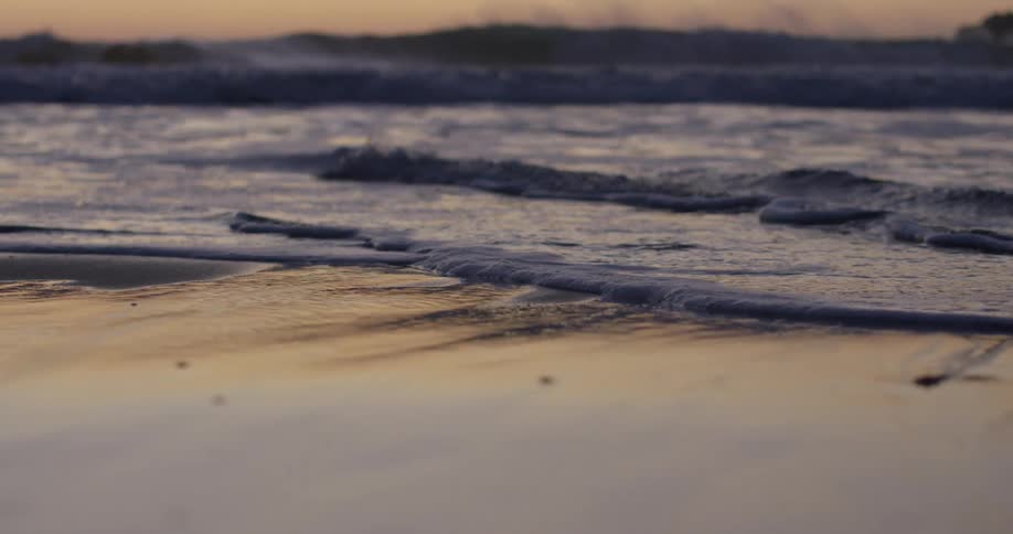 Small waves splash on the sandy shore as large waves curl and splash at sunset