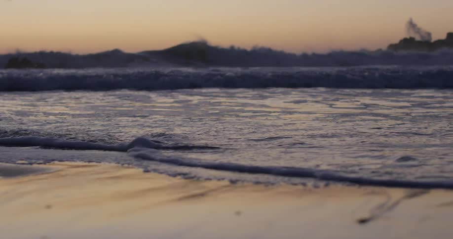 Ocean waves crashing on the sands in the shoreline of a beach at sunset