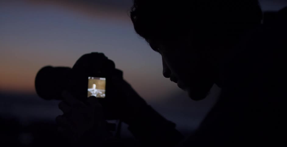 A man with a camera with the sky clouds and mountains in the background
