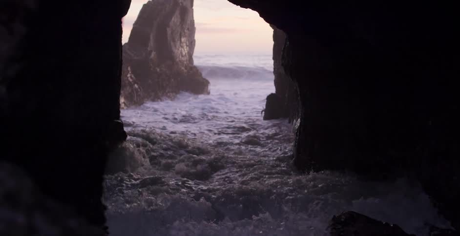 Ocean waves wash into a cave in a rock formation