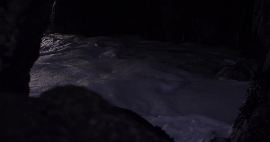 Strong waves crash onto rocks at the bottom of a cliff