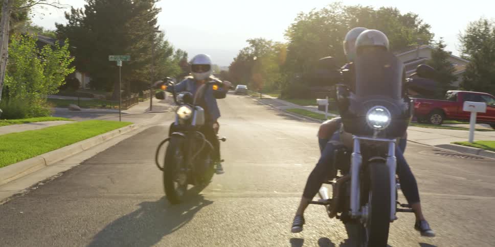 Female bikers ride their motorcycles through a suburban neighborhood