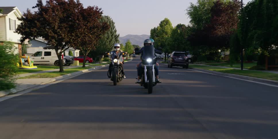 Two people are riding motorcycles through a suburban city