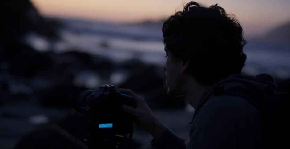 Photographer uses a camera on a tripod near the ocean at sunset