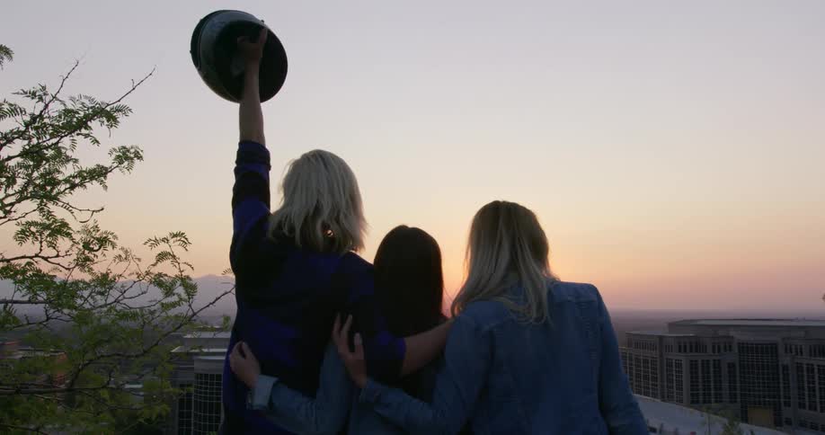 Three women hug while watching a sunset in a city