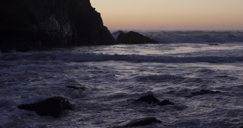 Red sky on horizon backs waves crashing against shore