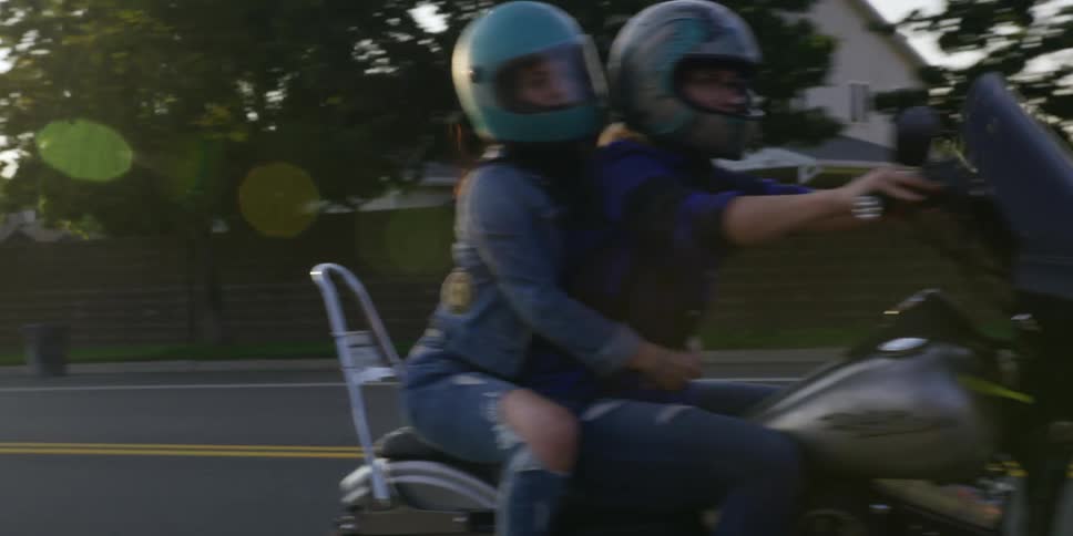 Couple of women with crash helmets drive a motorcycle on the road at morning