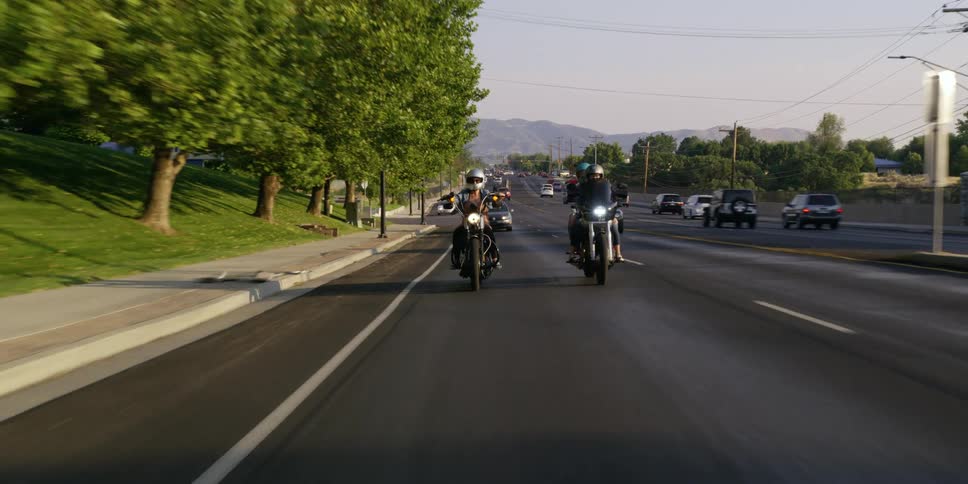 People driving motorcycles down a road with cars driving on it