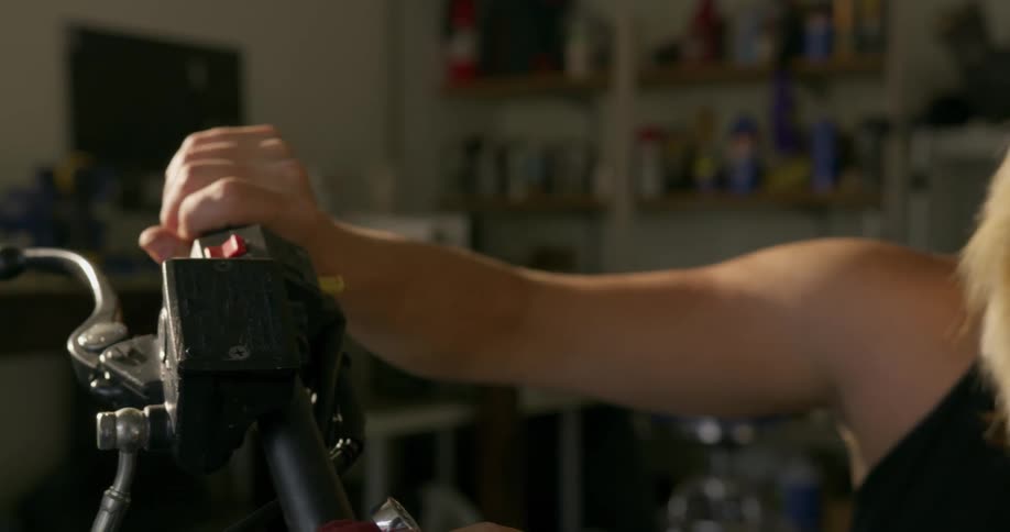 A woman turns the handle on her motorcycle in the garage