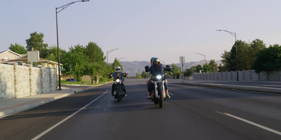 Two people ride motorcycles on a suburban highway