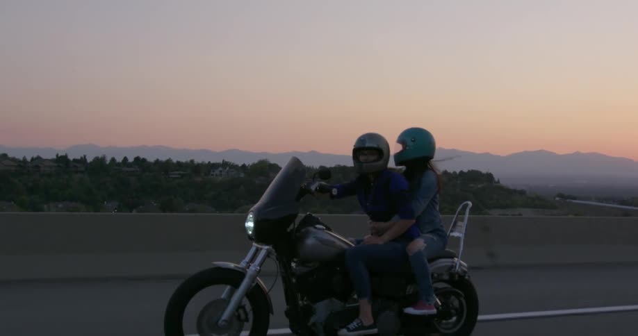 Couple of women ride motorcycle on the highway at sunset