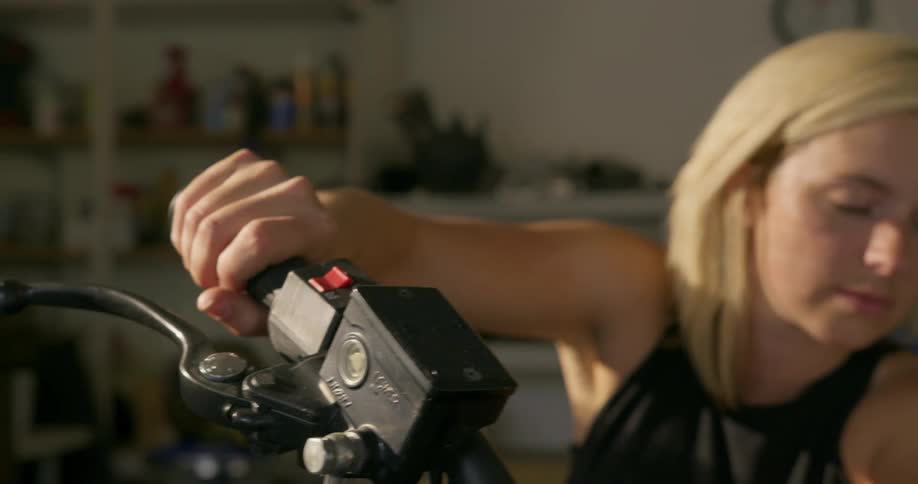 A woman in a garage sitting on a motorcycle and revving up the handle
