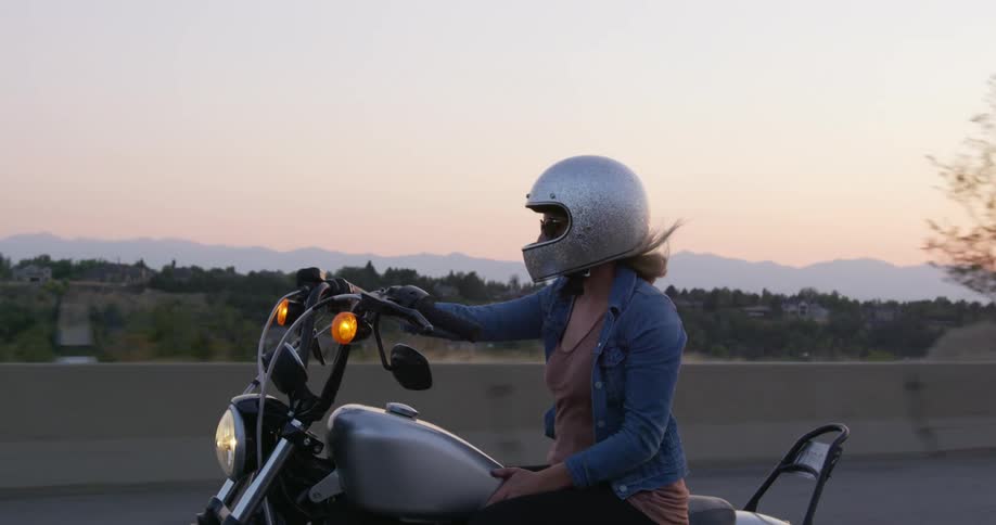 Woman wearing a crash helmet rides a motorcycle on the highway at sunset