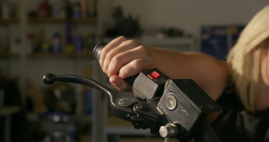 A woman in the garage sitting on a motorcycle revving up the handle