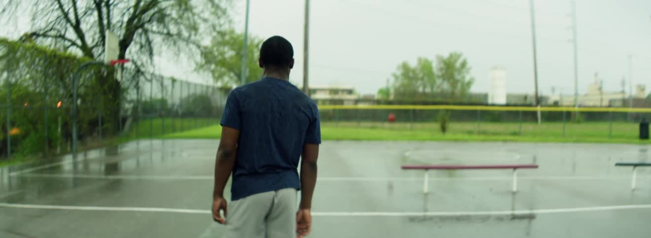 Man kicks a basketball on a wet outdoors court on an overcast day