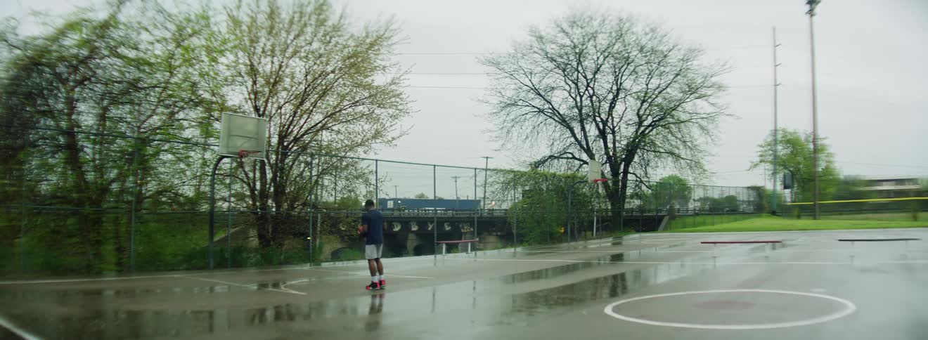 A male kicks a basketball across an outdoor court after missing throwing a basket