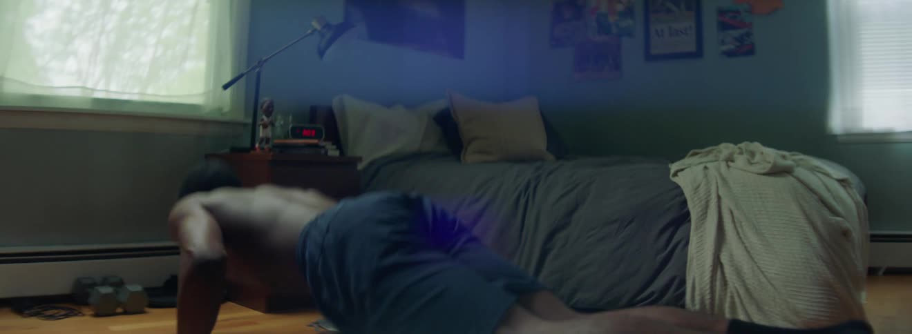 Shirtless black man pushes up by his bed in the room