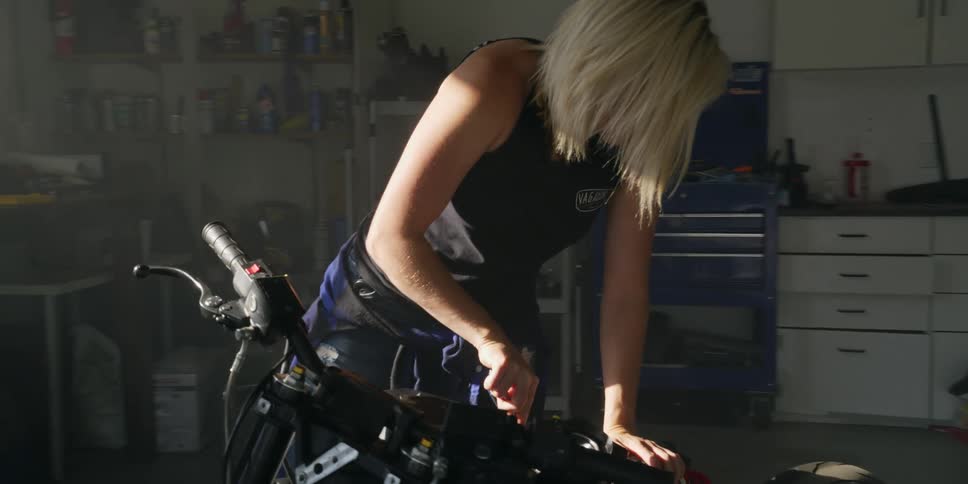 Blonde woman fixes a motorcycle inside a garage