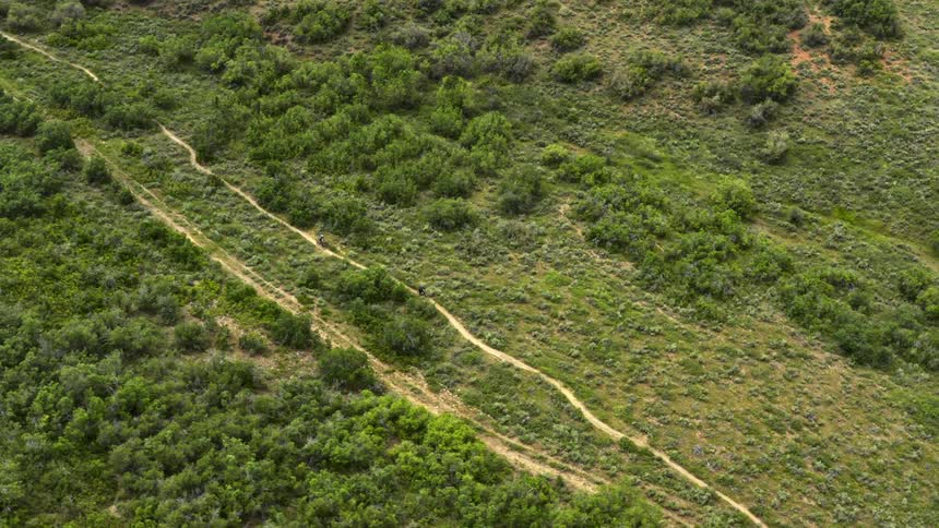 Aerial view of two cyclists riding bicycles down the dirt road through hills