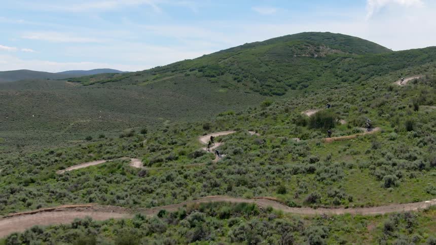 Bicyclist ride quickly along winding dirt road among green hills