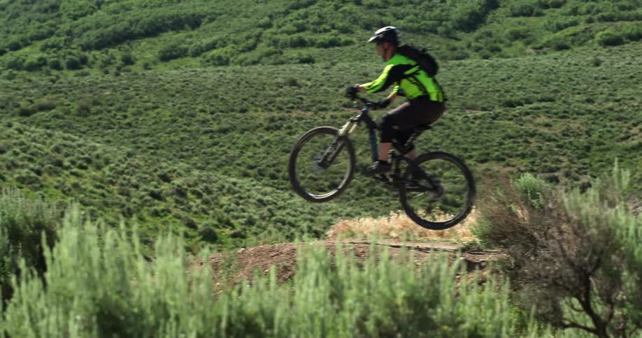 The wind blows the brush as a mountain bike rider rides on a hilly trail