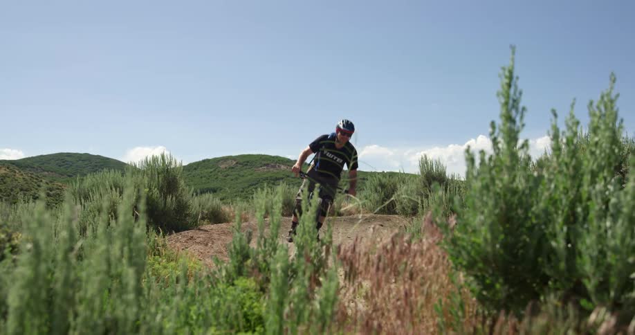A man rides a bike on a trail through brush on a bright sunny day