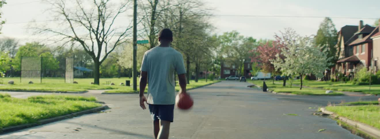 A teenager walks down a neighborhood street while dribbling a basketball