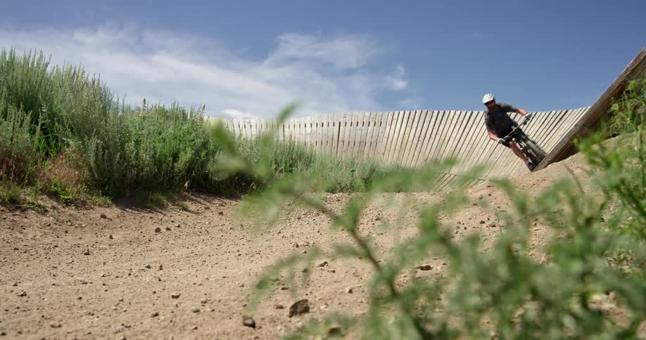 A person with a bicycle and a helmet riding on a fence with the sky and clouds in the background
