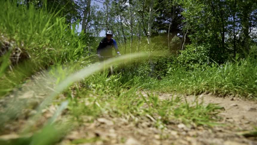 A cyclist with helmet and gloves rides a bicycle down a dirt road in the forest